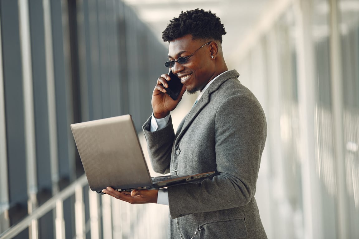 Confident businessman with laptop talking on smartphone in workplace